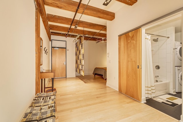 corridor with stacked washer and clothes dryer, beam ceiling, and light hardwood / wood-style flooring