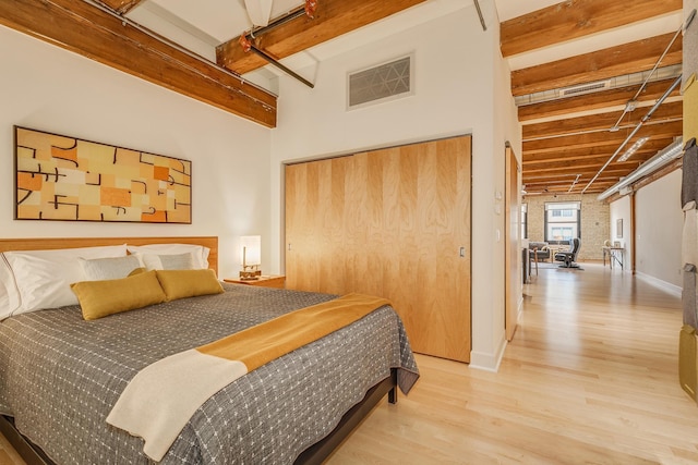 bedroom with light wood-type flooring, brick wall, beam ceiling, and a closet