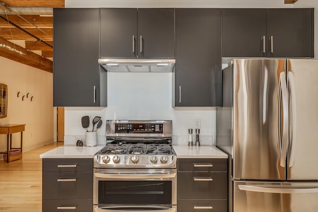 kitchen with light wood-type flooring, appliances with stainless steel finishes, beamed ceiling, and light stone countertops