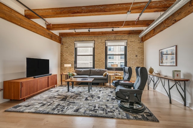 living room featuring light hardwood / wood-style flooring, beamed ceiling, and brick wall