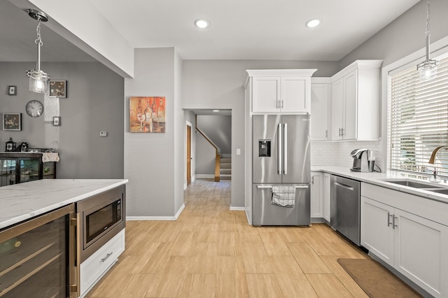 kitchen featuring sink, beverage cooler, white cabinetry, stainless steel appliances, and decorative light fixtures