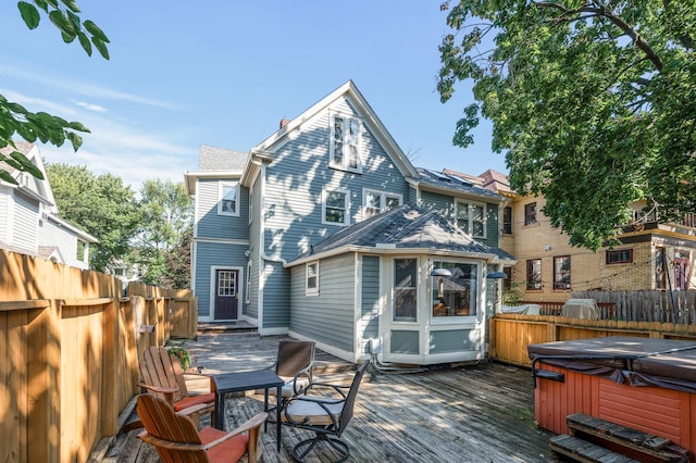 back of property with a wooden deck and a hot tub