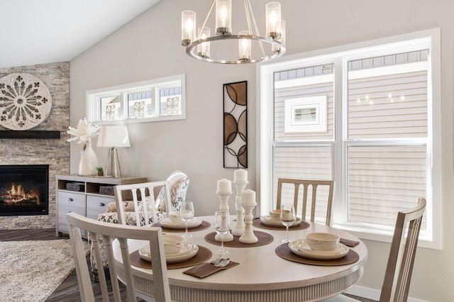 dining space with lofted ceiling, a stone fireplace, hardwood / wood-style floors, and a notable chandelier