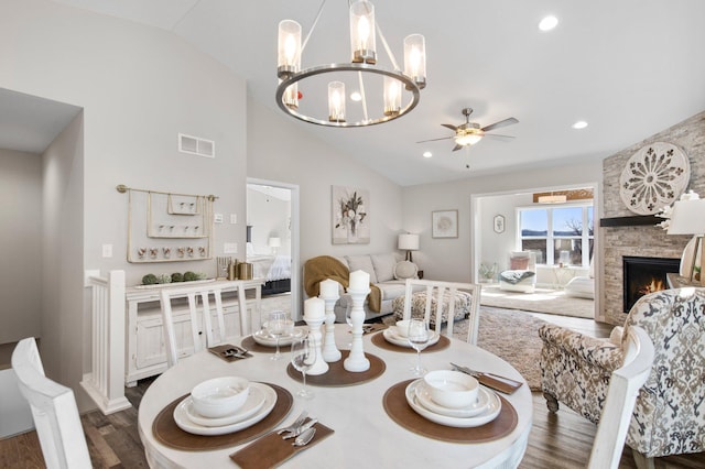 dining room with dark hardwood / wood-style floors, a fireplace, ceiling fan with notable chandelier, and vaulted ceiling