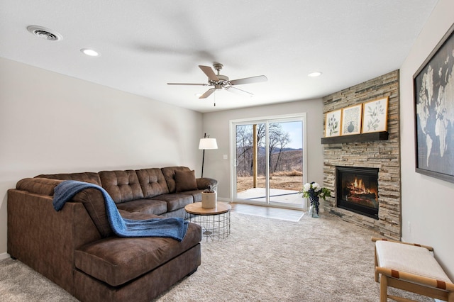 living room with a stone fireplace, ceiling fan, and carpet flooring