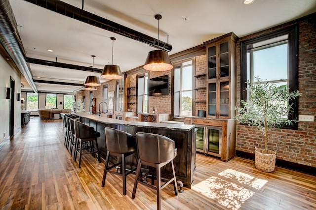 kitchen with a wealth of natural light, light hardwood / wood-style floors, hanging light fixtures, and brick wall