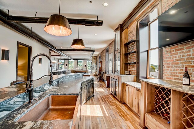 kitchen featuring brick wall, sink, dark stone countertops, light hardwood / wood-style floors, and hanging light fixtures