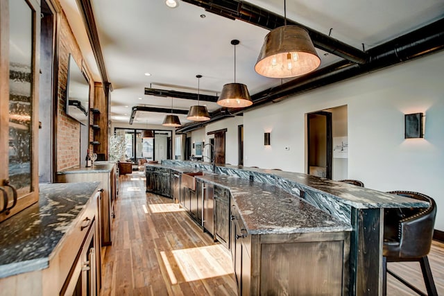 kitchen featuring light wood-type flooring, dark stone counters, sink, pendant lighting, and a breakfast bar area