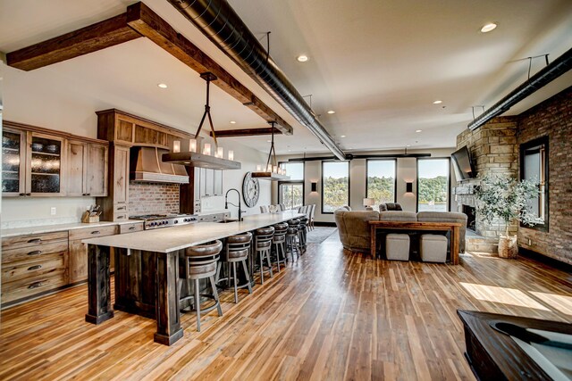 kitchen with custom range hood, pendant lighting, beamed ceiling, light hardwood / wood-style floors, and a stone fireplace