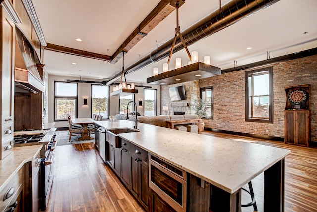 kitchen with brick wall, stainless steel appliances, sink, a large island with sink, and hardwood / wood-style flooring