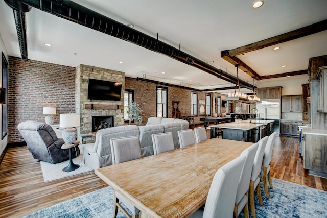 dining area with a fireplace, beam ceiling, dark hardwood / wood-style floors, and brick wall