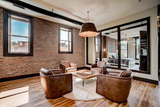 living room featuring a healthy amount of sunlight, brick wall, and wood-type flooring