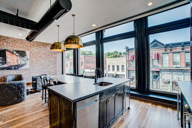 kitchen with sink, brick wall, pendant lighting, light hardwood / wood-style floors, and a center island with sink