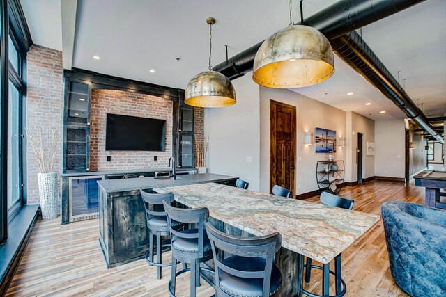 kitchen with decorative light fixtures, a kitchen bar, wine cooler, and light hardwood / wood-style flooring