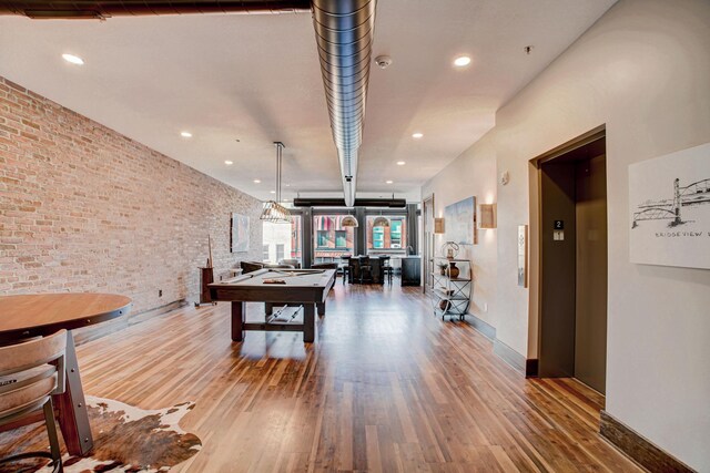 recreation room with billiards, brick wall, wood-type flooring, and elevator