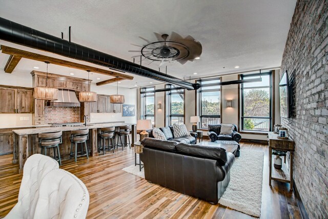 living room with ceiling fan, a textured ceiling, beam ceiling, light hardwood / wood-style floors, and brick wall