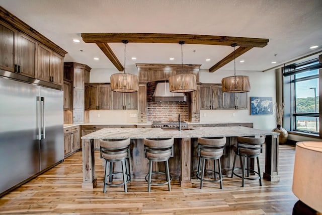 kitchen featuring pendant lighting, wall chimney exhaust hood, light wood-type flooring, appliances with stainless steel finishes, and a large island