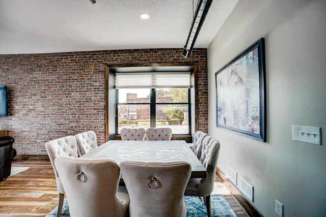 dining space with hardwood / wood-style floors, a textured ceiling, and brick wall