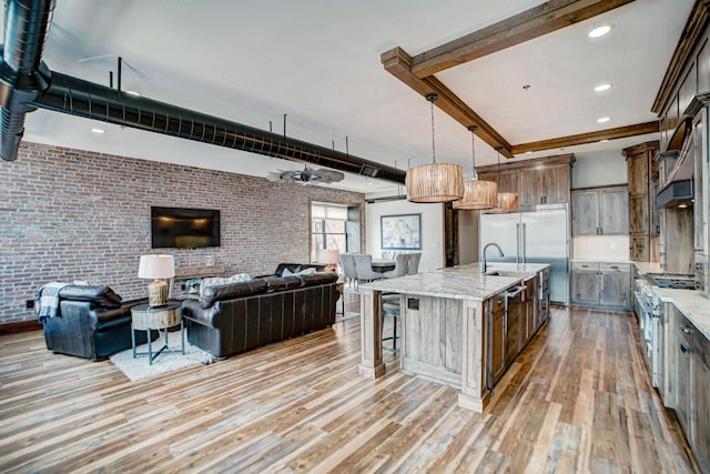 kitchen with light stone countertops, a large island, light hardwood / wood-style flooring, brick wall, and decorative light fixtures