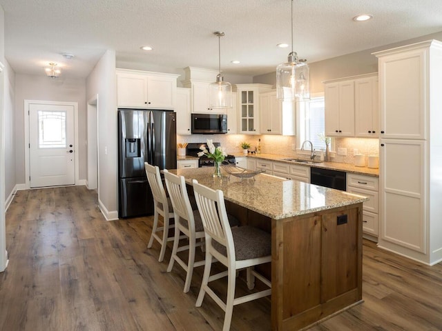 kitchen with dark wood-type flooring, black appliances, a kitchen island, and white cabinetry