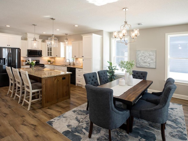 dining space featuring a healthy amount of sunlight, sink, a notable chandelier, and dark wood-type flooring