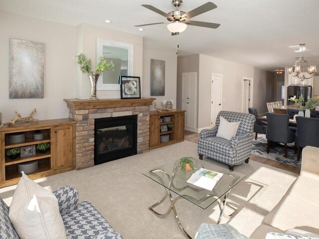 carpeted living room with ceiling fan with notable chandelier and a fireplace