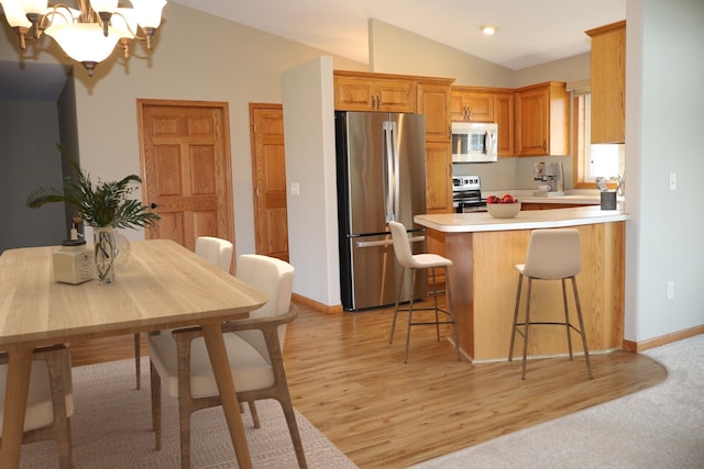 kitchen with light wood-type flooring, kitchen peninsula, stainless steel appliances, vaulted ceiling, and a breakfast bar