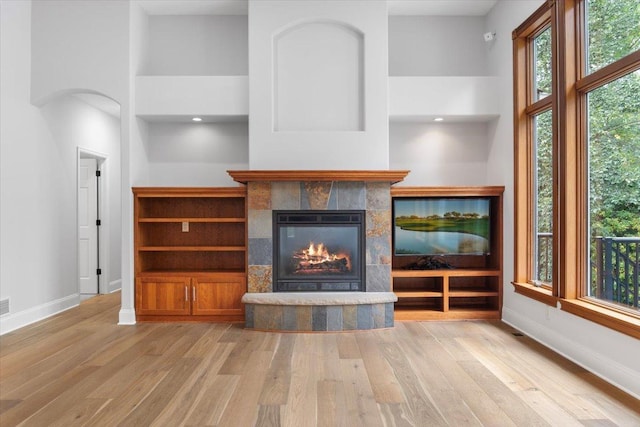 unfurnished living room with light hardwood / wood-style floors, a high ceiling, and a tiled fireplace