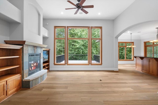 unfurnished living room featuring ceiling fan with notable chandelier, a tiled fireplace, and light wood-type flooring