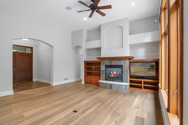 unfurnished living room featuring ceiling fan, a tiled fireplace, and light wood-type flooring