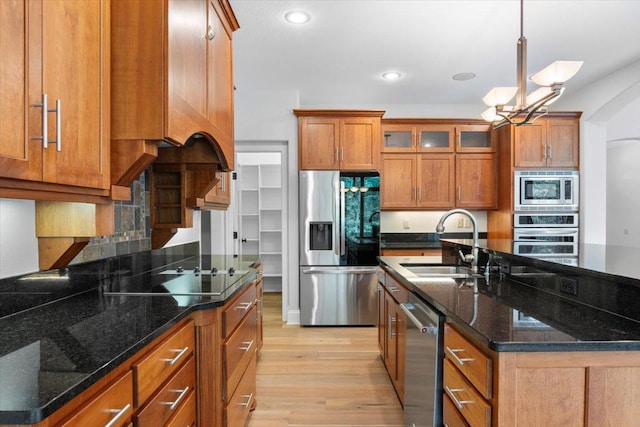 kitchen featuring decorative light fixtures, sink, light hardwood / wood-style flooring, stainless steel appliances, and dark stone counters