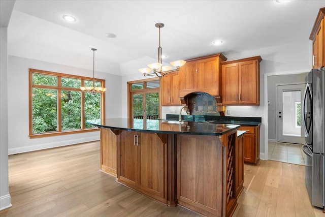 kitchen featuring a center island with sink, a notable chandelier, light wood-type flooring, hanging light fixtures, and stainless steel refrigerator