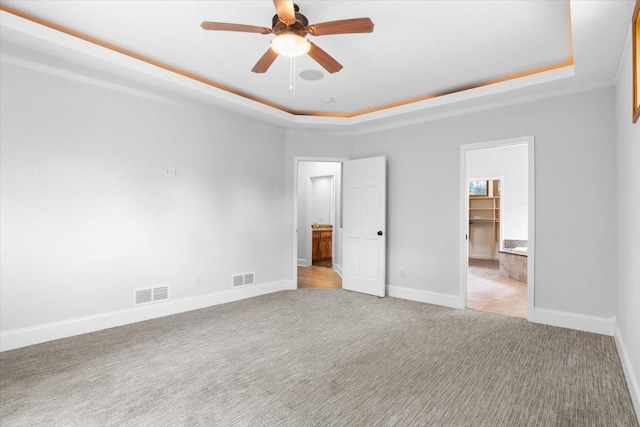 unfurnished bedroom featuring ceiling fan, a walk in closet, light colored carpet, and a tray ceiling