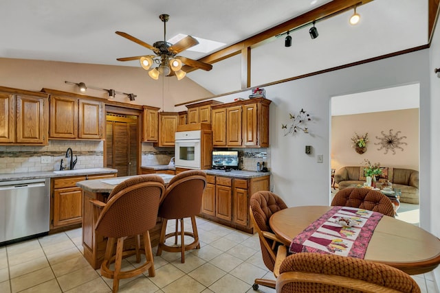 kitchen with backsplash, white oven, lofted ceiling with skylight, ceiling fan, and stainless steel dishwasher