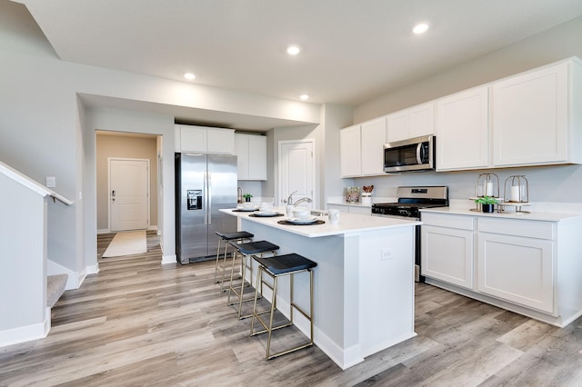 kitchen featuring white cabinetry, light hardwood / wood-style flooring, a kitchen bar, stainless steel appliances, and a center island with sink