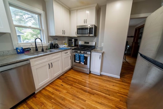 kitchen with light stone countertops, stainless steel appliances, sink, light hardwood / wood-style flooring, and white cabinets