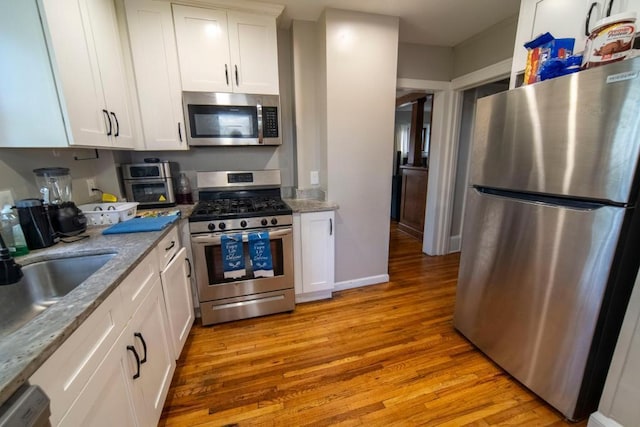 kitchen featuring white cabinets, sink, light stone countertops, light wood-type flooring, and appliances with stainless steel finishes