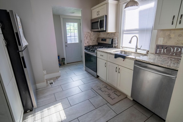 kitchen with light stone countertops, sink, tasteful backsplash, white cabinets, and appliances with stainless steel finishes