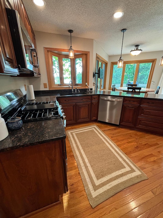 kitchen with gas range oven, sink, hanging light fixtures, stainless steel dishwasher, and light hardwood / wood-style floors