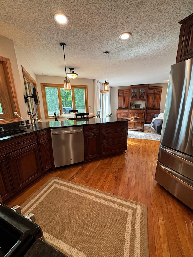 kitchen with light hardwood / wood-style flooring, decorative light fixtures, appliances with stainless steel finishes, kitchen peninsula, and a textured ceiling