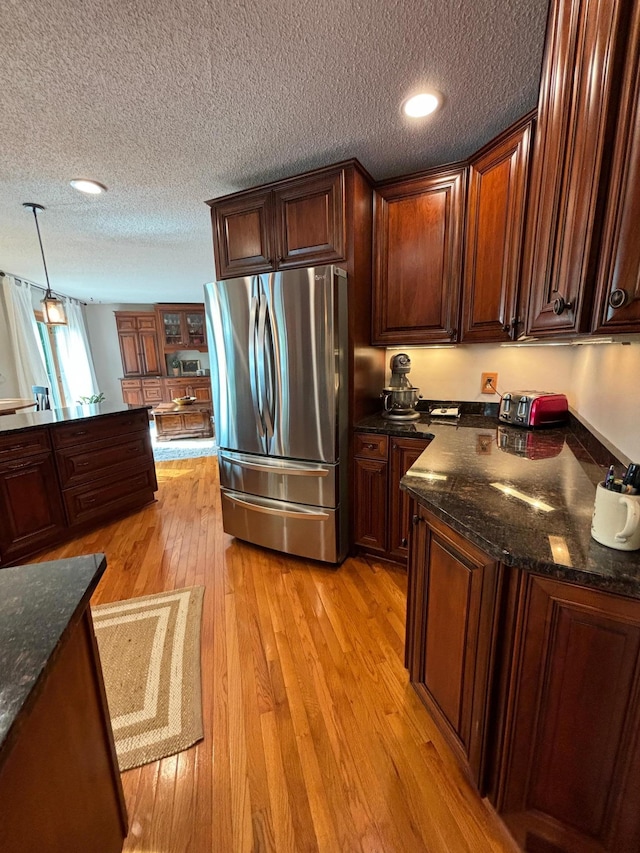 kitchen featuring a textured ceiling, pendant lighting, stainless steel refrigerator, and light wood-type flooring
