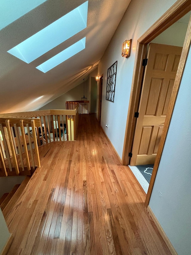 corridor with vaulted ceiling with skylight and wood-type flooring