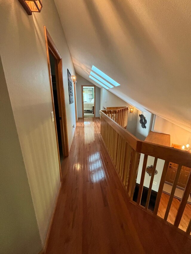hall featuring a textured ceiling, hardwood / wood-style floors, and lofted ceiling with skylight