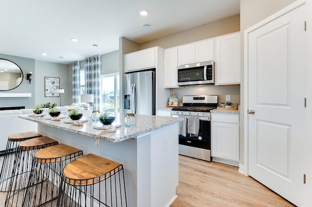 kitchen featuring white cabinets, a center island, light hardwood / wood-style flooring, appliances with stainless steel finishes, and a kitchen breakfast bar