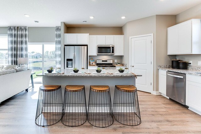 kitchen with a center island, light hardwood / wood-style flooring, appliances with stainless steel finishes, light stone counters, and a breakfast bar area