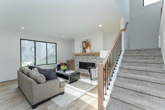 living area featuring light wood-style flooring, recessed lighting, a stone fireplace, and stairway