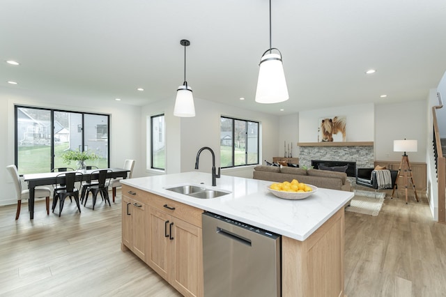 kitchen featuring a sink, light wood-style floors, stainless steel dishwasher, light brown cabinetry, and a center island with sink