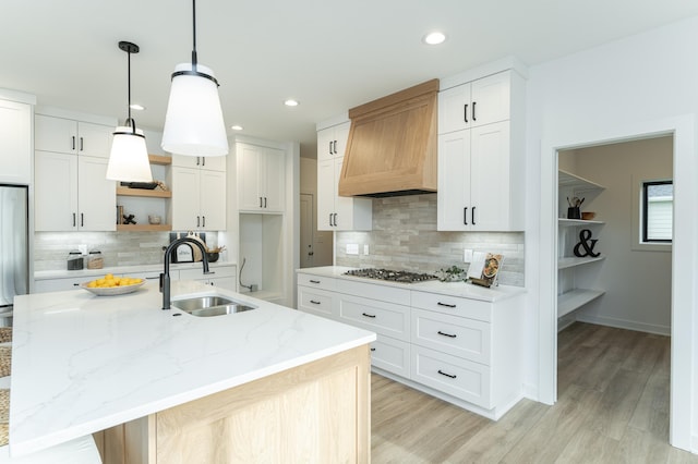 kitchen with open shelves, appliances with stainless steel finishes, light wood-style floors, a sink, and premium range hood