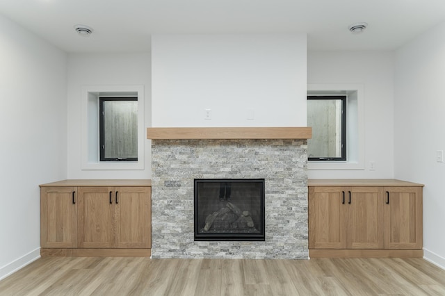 unfurnished living room featuring light wood-type flooring, a stone fireplace, and baseboards