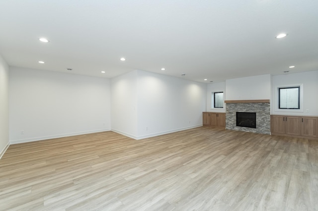 unfurnished living room with recessed lighting, a stone fireplace, and light wood finished floors